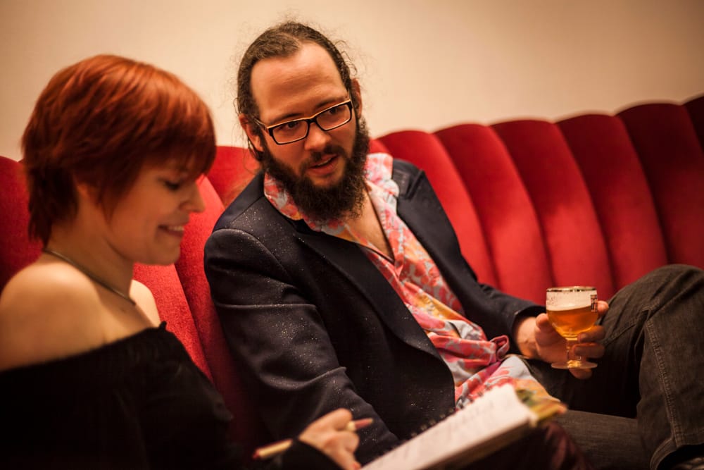 Nicolas Monfort, une Chimay à la main, doit être en train de dire une blague à Clotilde Delcommune qui l'interviewe, vu le sourire en coin de l'une et l'air taquin de l'autre.