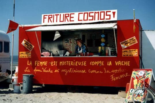 Une baraque à frites intitulées "Friture Cosmos" sur laquelle est tagué "La femme est mystérieuse comme la vache" et en-dessous "La vache est mystérieuse comme la femme". Scène de Camping Cosmos de Jan Bucquoy.